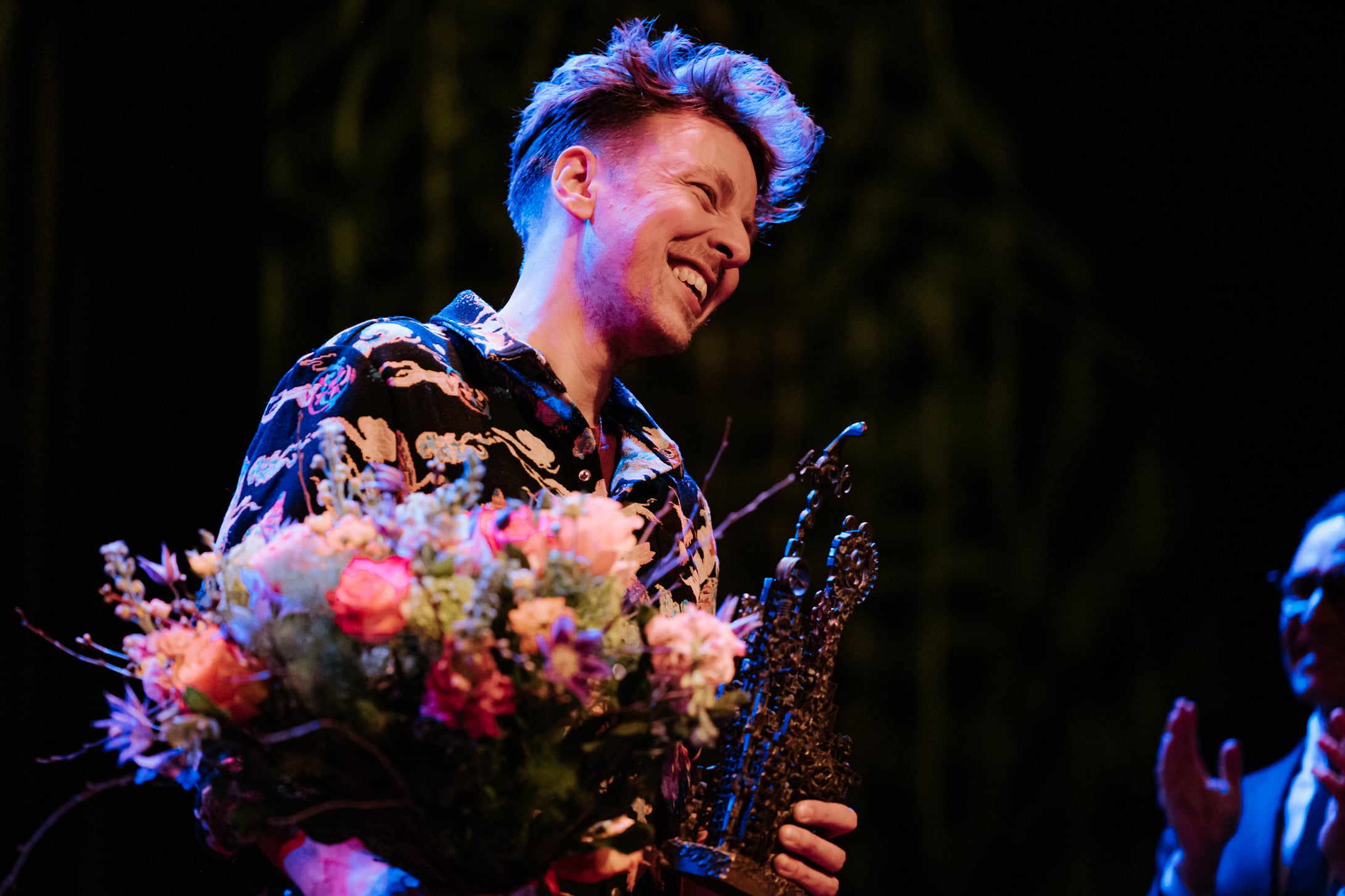 Reinier Baas lachend met een bos bloemen en de John Coltrane wisselsculptuur van Jan Wolkers