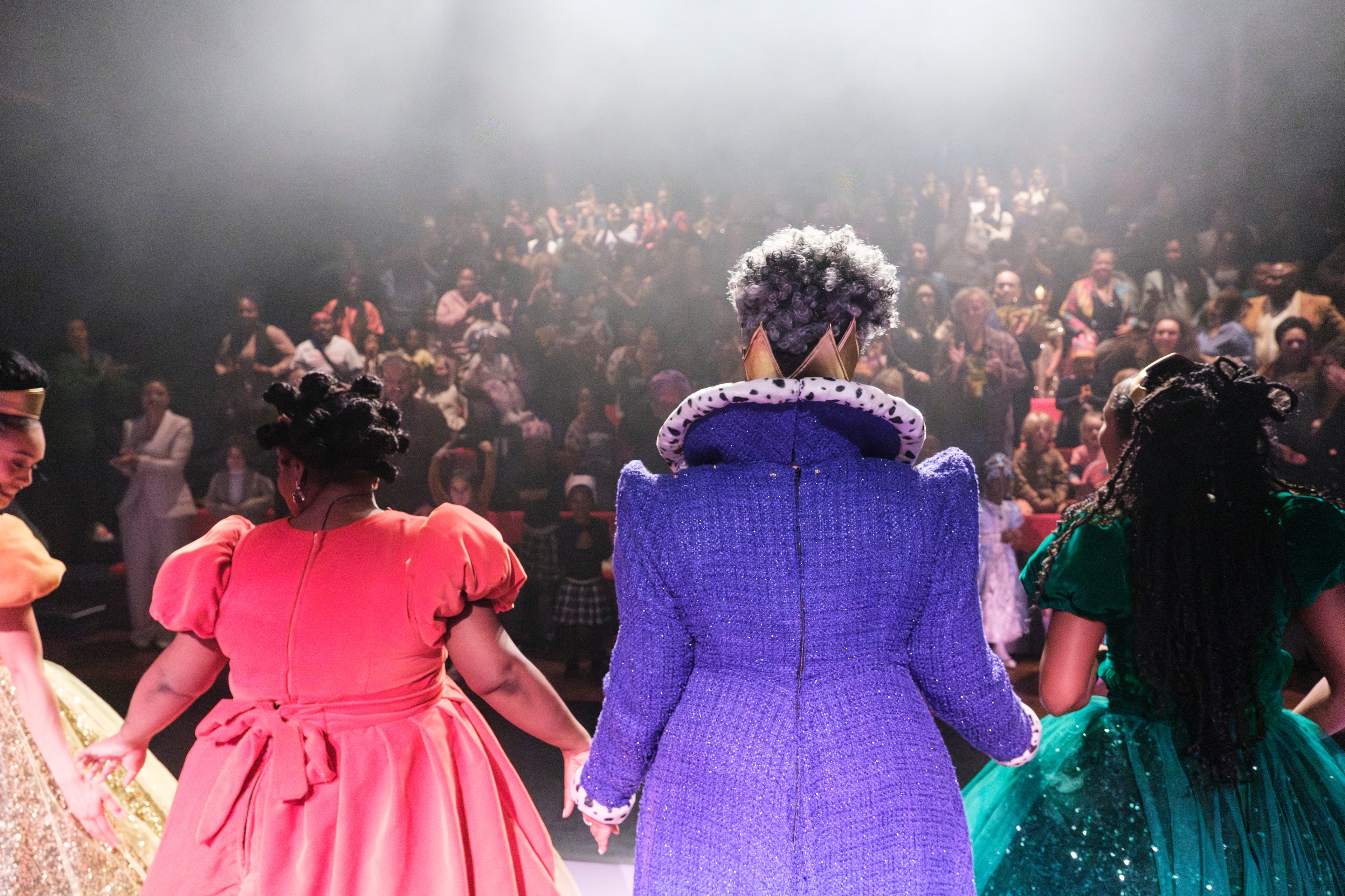 Acteurs in kleurrijke kostuums staan hand in hand op een podium en buigen naar het publiek.