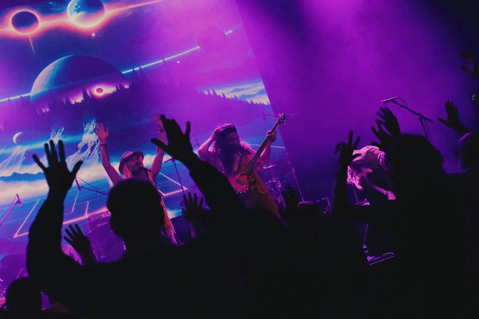 Band speelt op een podium met kleurrijke lichten terwijl het publiek met handen omhoog meedoet.